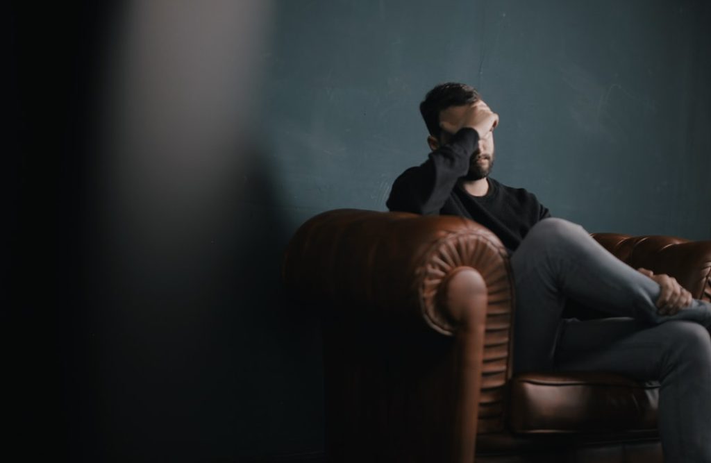 depressed, anxious man holds his head while sitting on a sofa